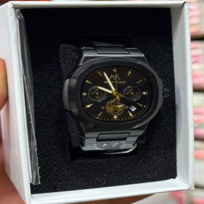 A black analog watch with a gold-tone skeleton dial and gold hands is displayed inside a white presentation box held by a hand. The background shows a blurred retail store setting with shelves of similar boxes.