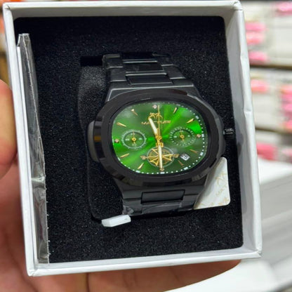 A black analog watch with a vibrant green dial and gold-tone details, presented inside its white retail box and held by a hand. The background shows a blurred retail store setting with shelves and calculators.
