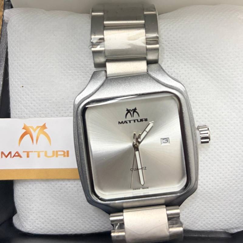 A silver-tone stainless steel analog watch with a square bezel and matching metal link bracelet, resting on a white textured cushion. The watch face is silver with a date window and the brand name 'MATTURI' printed on it.