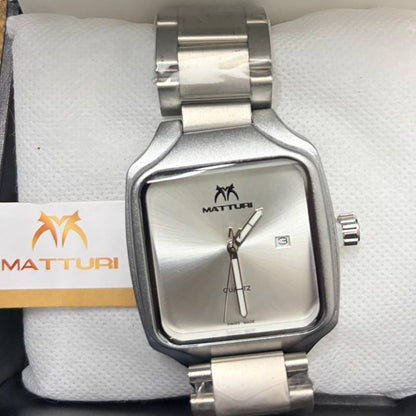 A silver-tone stainless steel analog watch with a square bezel and matching metal link bracelet, resting on a white textured cushion. The watch face is silver with a date window and the brand name 'MATTURI' printed on it.